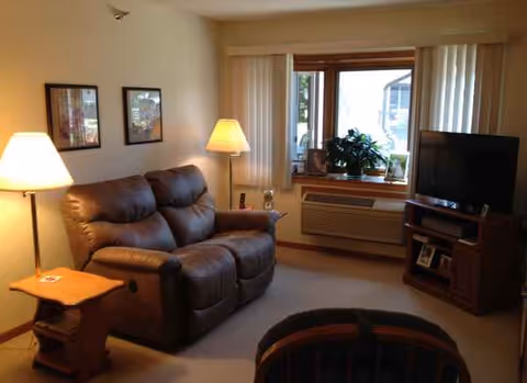 Cozy senior living living room with a leather sofa, lamps, TV, and a large window.