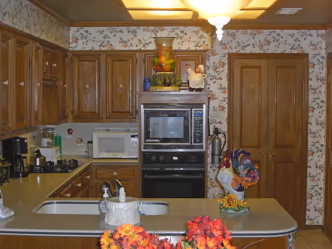 Cozy kitchen with wooden cabinets, built-in oven, microwave, and colorful flowers on the counter.