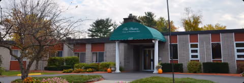 Single-story senior living facility entrance with a green awning and landscaped grounds.