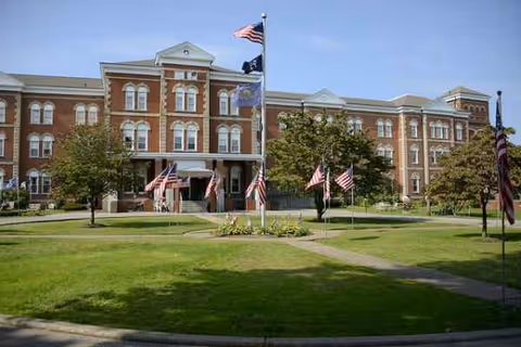 Brick senior living facility front view with American flags and a manicured lawn.
