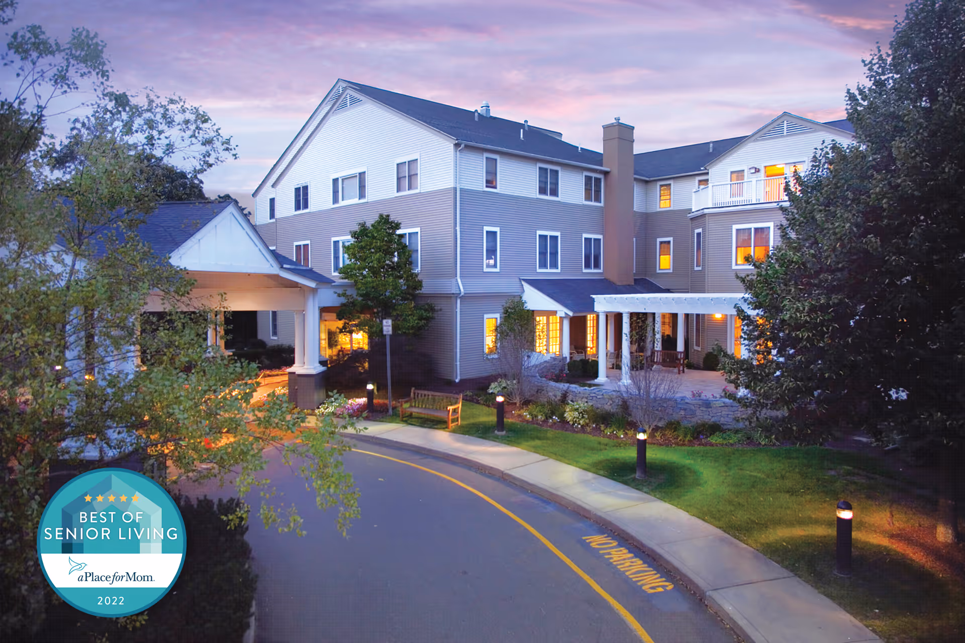 Exterior view of Maplewood at Orange with the building entrance, curved driveway, and landscaped grounds at dusk.