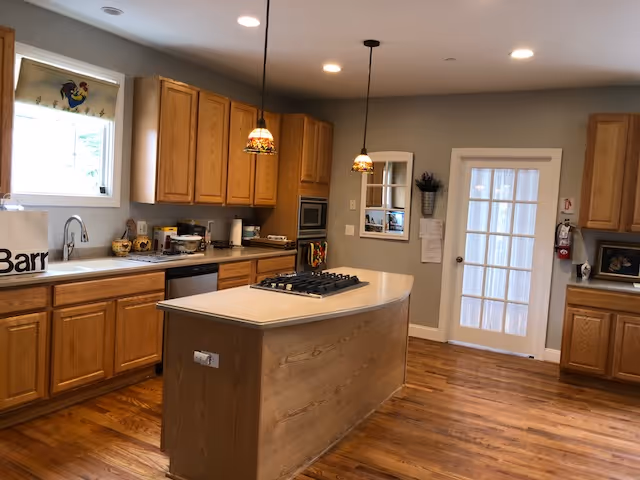 Bright kitchen with wooden cabinets, island, appliances, and pendant lights in a senior living facility.