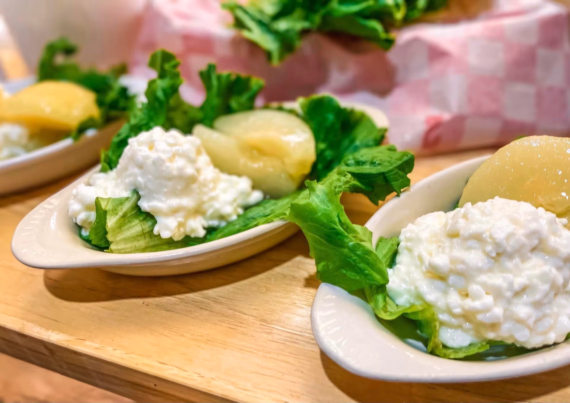 Small oval dishes with cottage cheese on lettuce and peach halves arranged on a wooden table.
