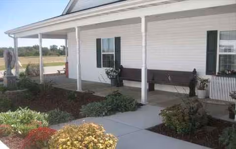 Exterior view of a white brick senior living facility with a porch and benches.