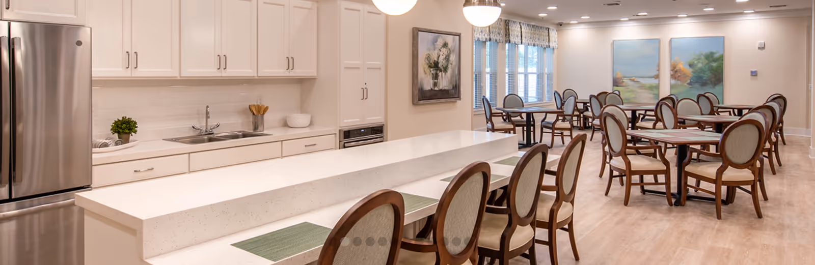 Open communal dining area with a kitchen island, bar seating, and multiple round dining tables and chairs.