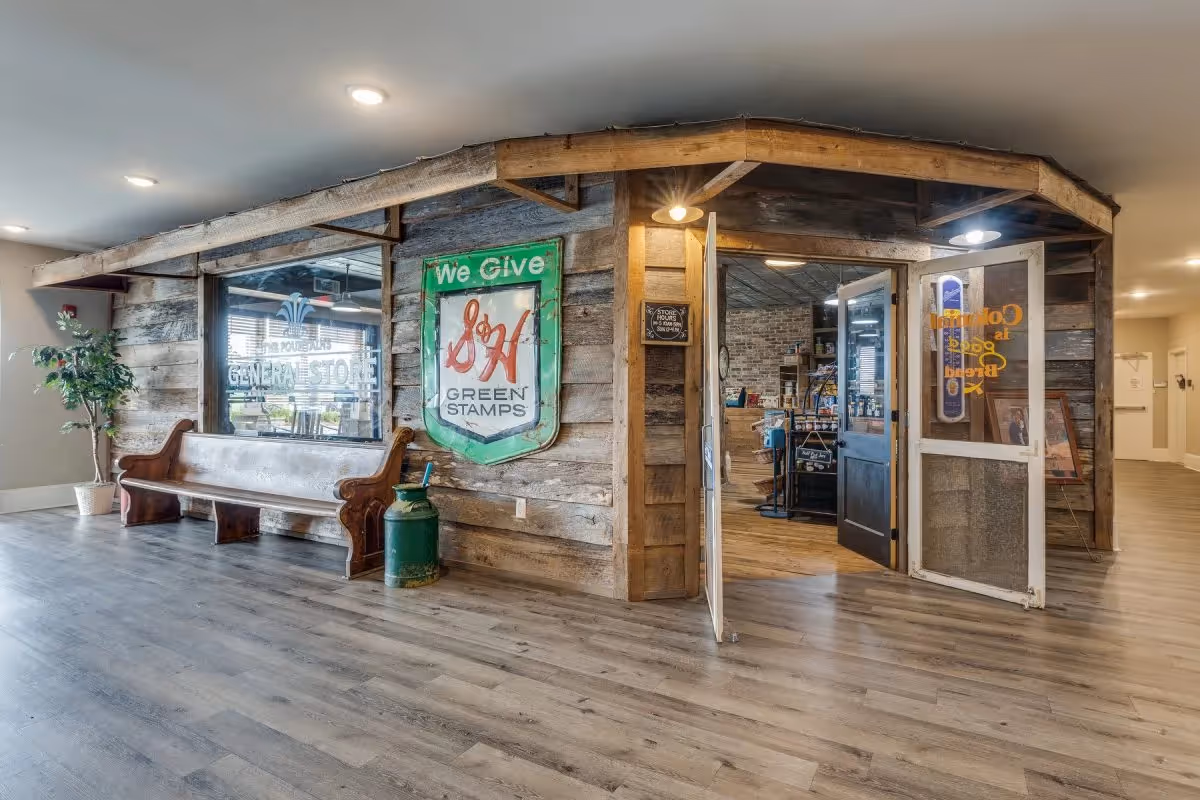 Indoor rustic general-store style room with reclaimed wood walls, a wooden bench, a 'Green Stamps' sign, and open doors into a shop area.