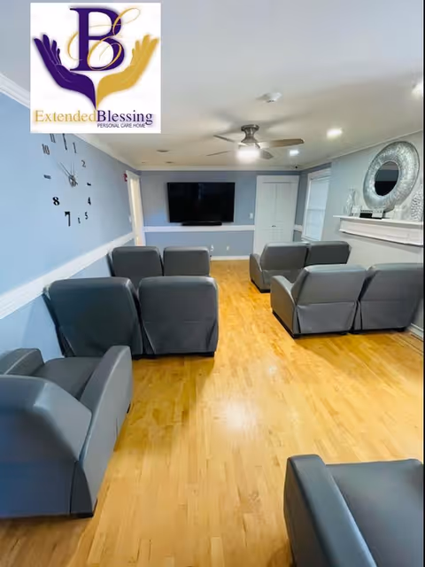 Common room with rows of gray recliner chairs facing a wall-mounted TV in a senior living facility.