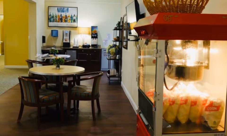 Community snack area with round tables and chairs, a popcorn machine in the foreground and a beverage station in the background.