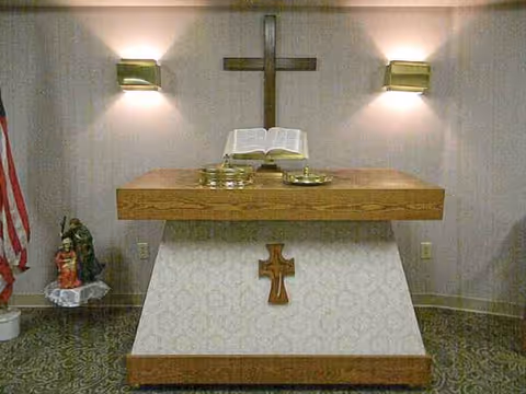 Altar with cross, open Bible, candles, and statue in a care center chapel.