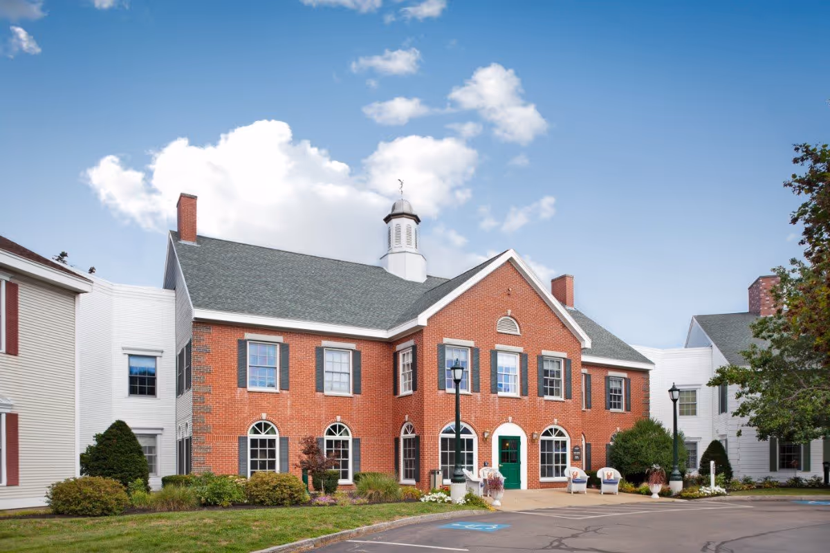 Front exterior of a two-story red brick building with white side wings, a cupola, and a landscaped entrance.