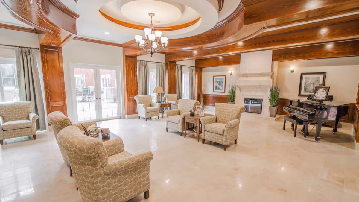 Bright, elegant lounge with upholstered armchairs arranged around tables, a fireplace and a grand piano under a decorative ceiling.