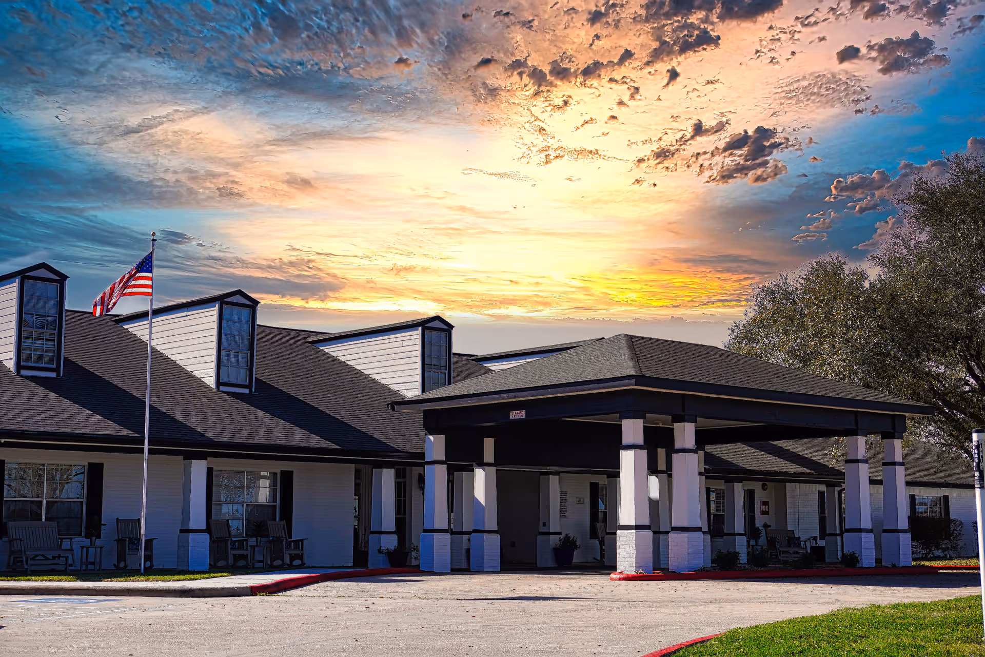 Front exterior of a senior living facility with a covered entrance and American flag