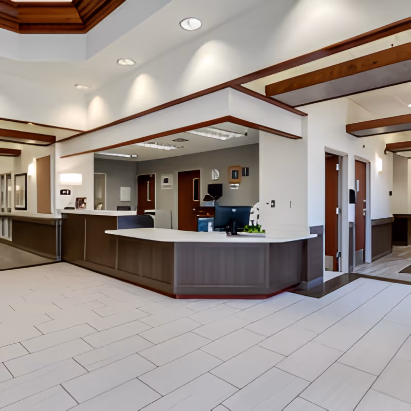 Reception area inside Monument Health Murray Creek facility with a large counter, computer, and several doors leading to other rooms. The space features white walls, wood trim accents, and tiled flooring.