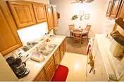 Small kitchen with wooden cabinets, sink and appliances opening onto a cozy round dining table with chairs.