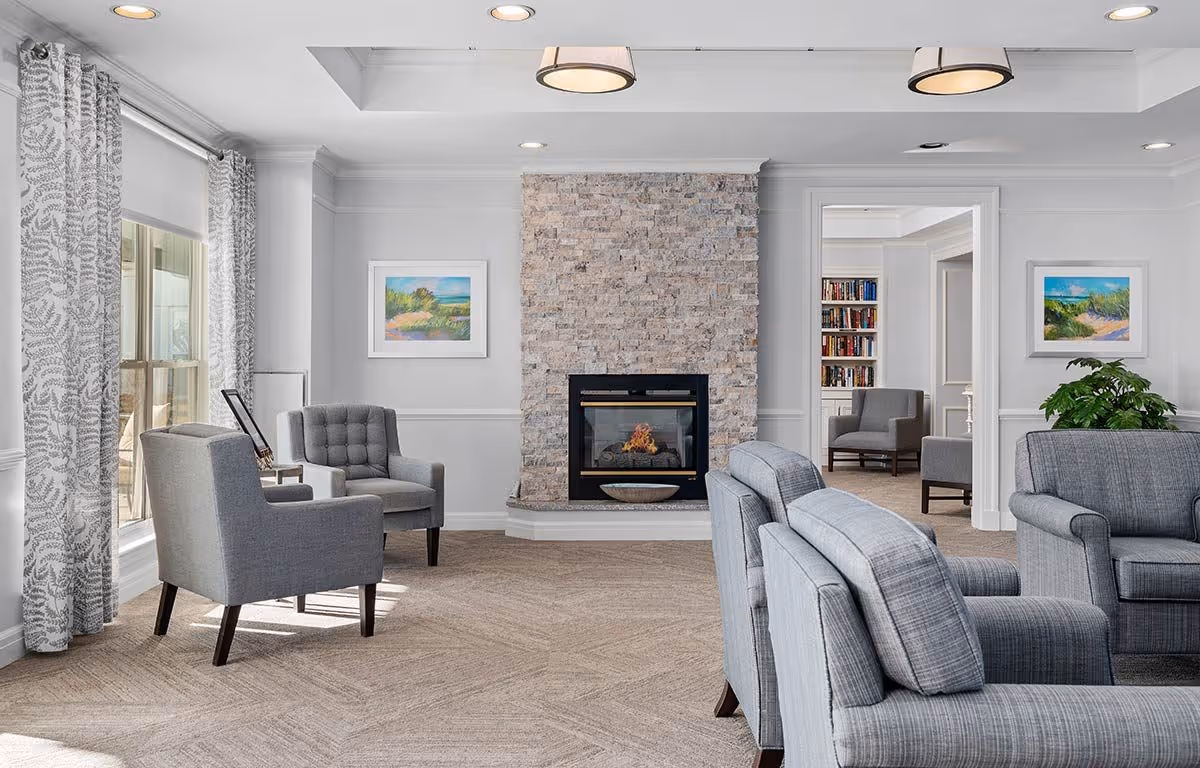 Bright communal living room with gray upholstered chairs arranged around a stone fireplace