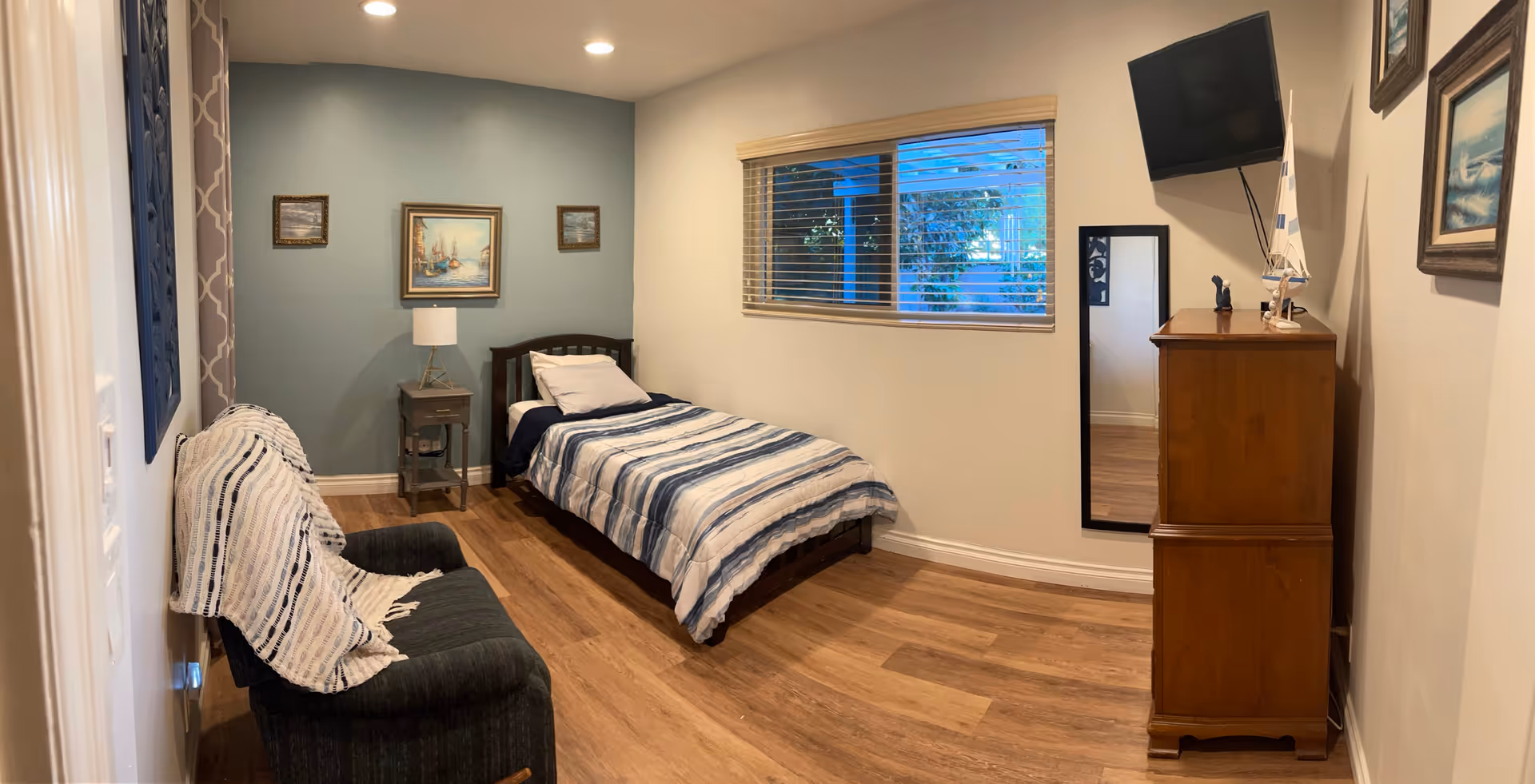 A cozy bedroom in a senior living facility with bed, dresser, and chair.