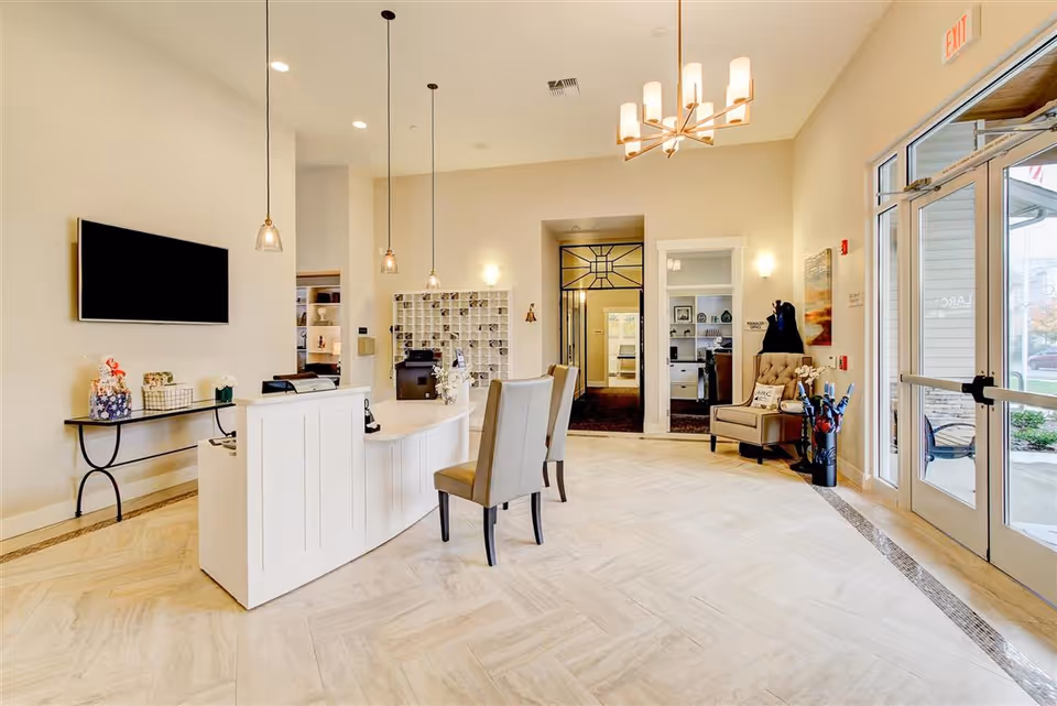 Bright reception lobby with a white curved front desk, seating, pendant lights, and glass entrance doors.