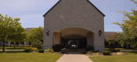 Brick senior living facility with a covered front entrance and landscaped path.