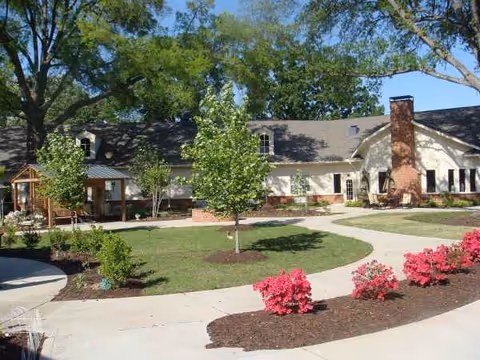 Exterior view of Apple Grove Alzheimer's Residence with curved path, lawn, trees, and pink shrubs.