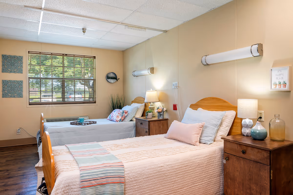 A well-furnished shared bedroom in a senior living facility featuring two beds, nightstands, and decorative elements.