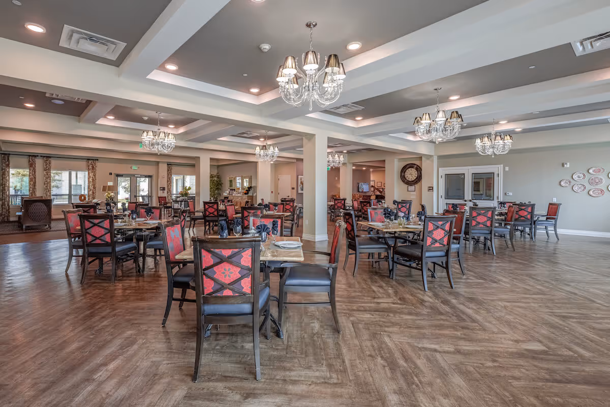 Spacious dining room with multiple round tables and red-upholstered chairs under chandeliers.