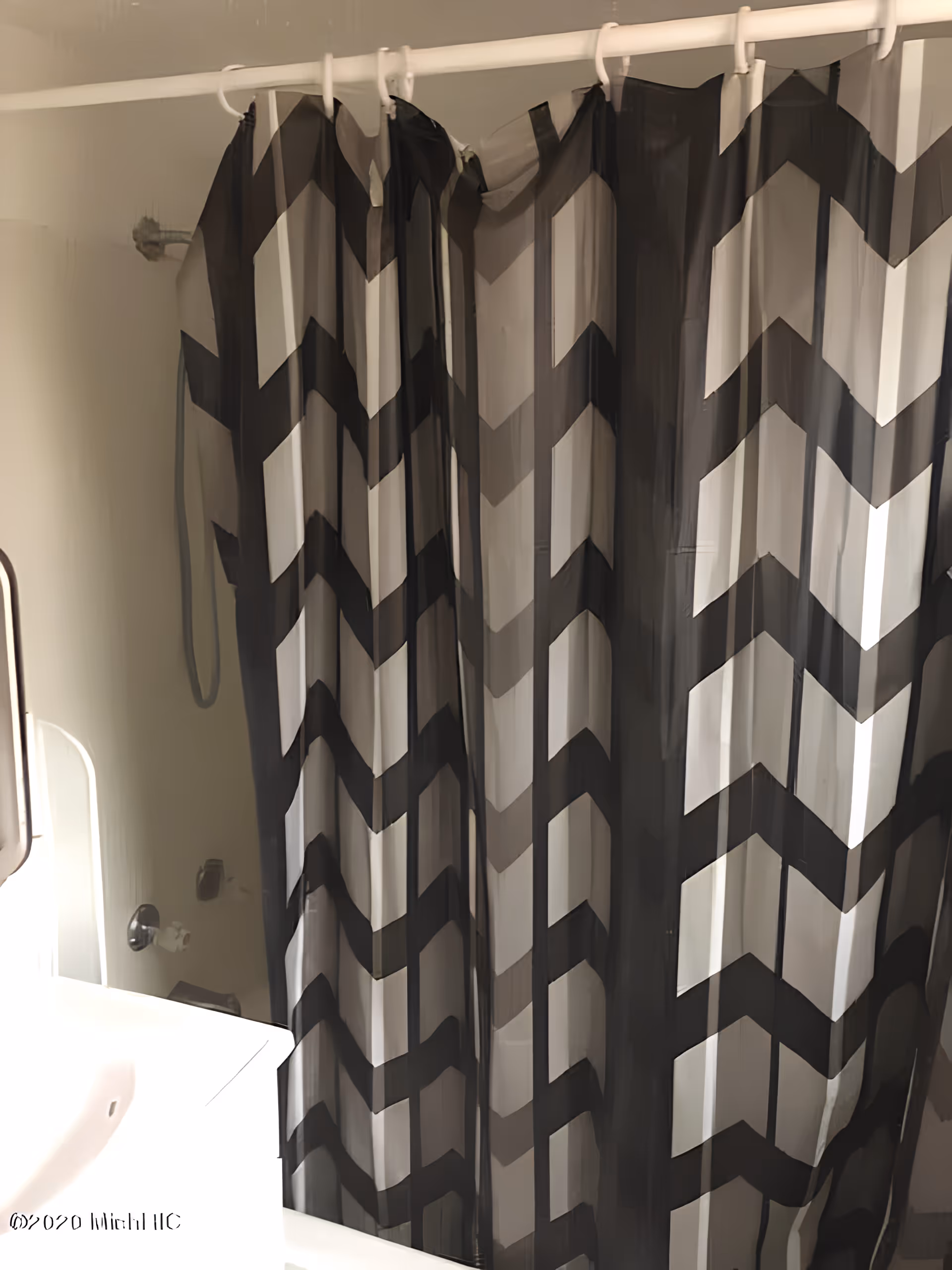 Shower with a black-and-white chevron patterned curtain and a partial bathroom sink visible on the left.