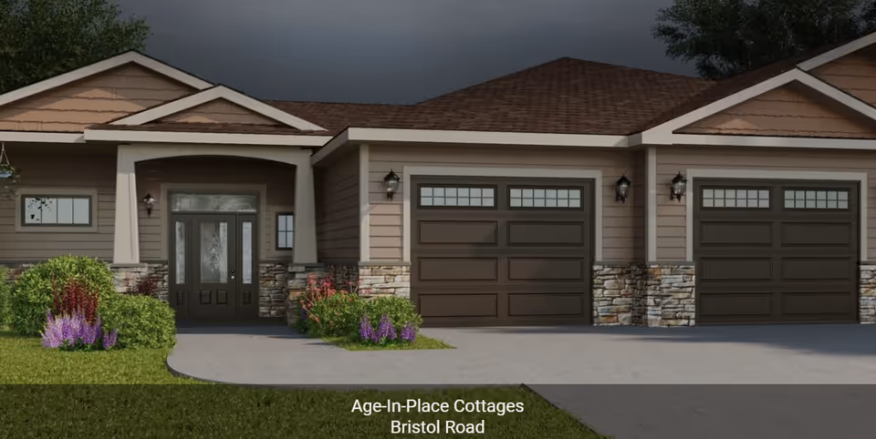Exterior view of a single-story cottage with a covered entrance, two garage doors, stone and wood siding, and landscaped bushes and flowers in front.
