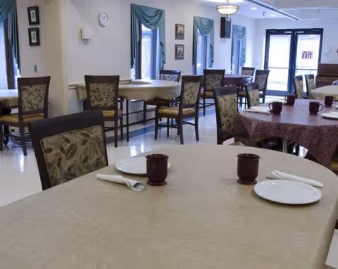 Senior living dining room with empty tables set with plates and mugs.