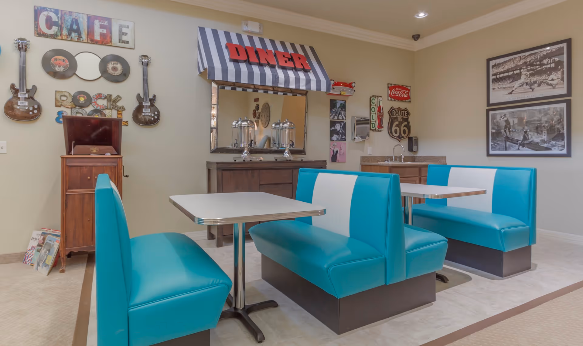 Interior view of a retro-themed dining area with turquoise and white diner booths, a table, and vintage decor including guitars, vinyl records, a 'DINER' sign with a striped awning, and Route 66 memorabilia on the walls.