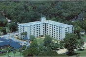 Aerial view of Hugh Ash Manor, a multi-story residential building surrounded by trees and greenery, with a parking lot visible on the left side.