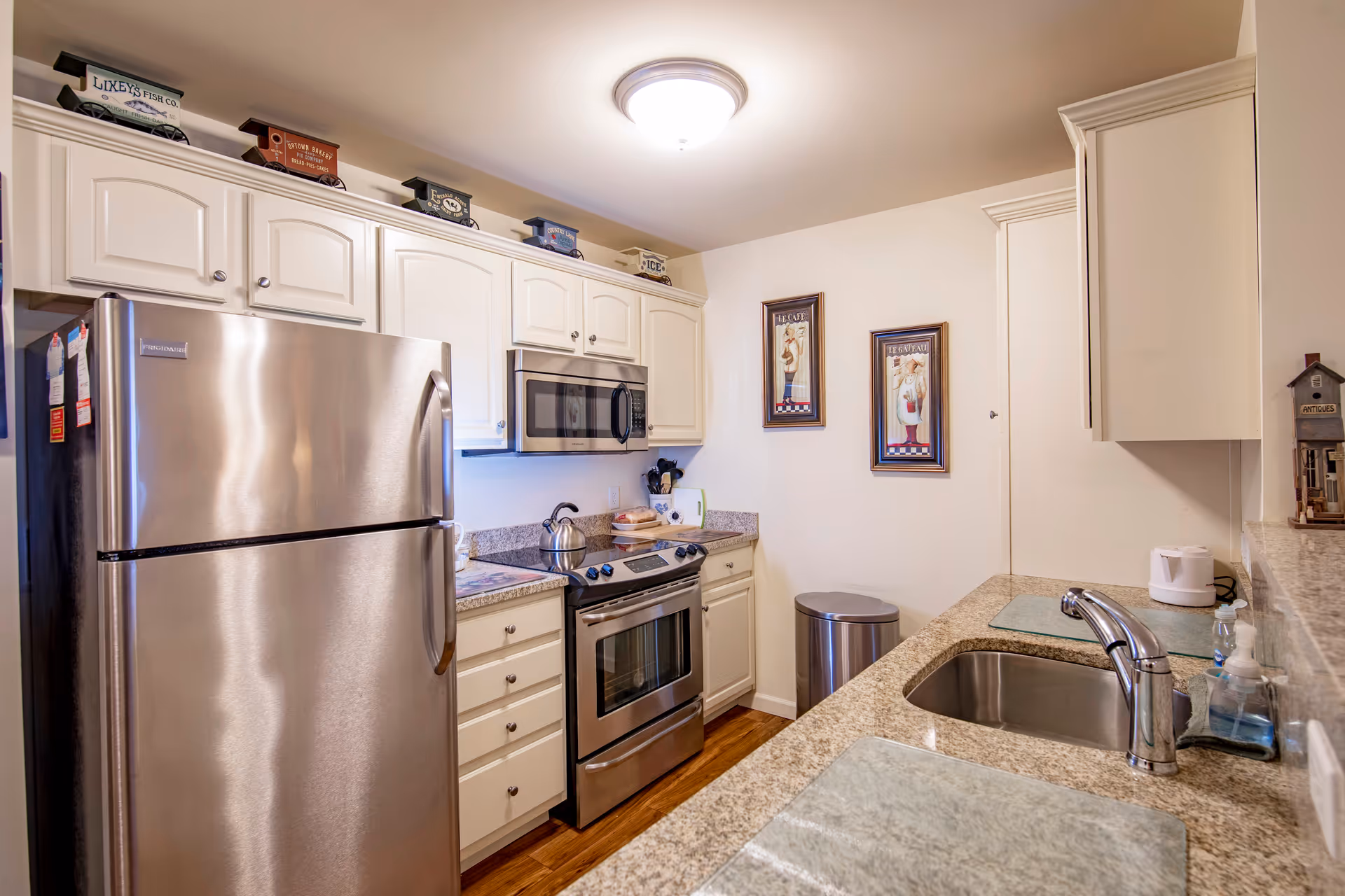 Bright kitchen with stainless steel refrigerator, oven and microwave, granite countertops, a sink, and white cabinets.