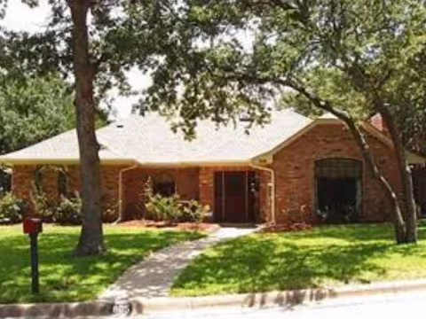 Front view of a single-story brick residential care home with a walkway and trees.