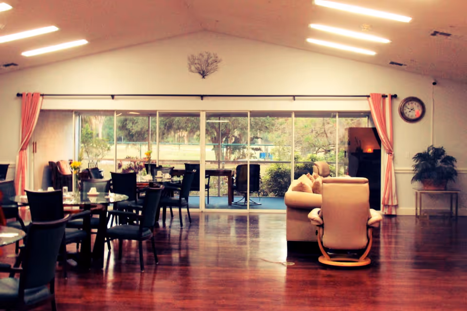 Spacious senior living dining area with round dining tables and chairs and a lounge seating area facing large sliding glass doors to a garden.