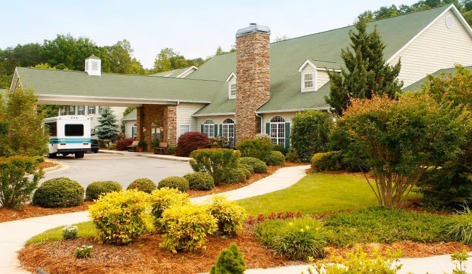 A landscaped entrance to Brasstown Manor Senior Living facility featuring a stone chimney and lush greenery.
