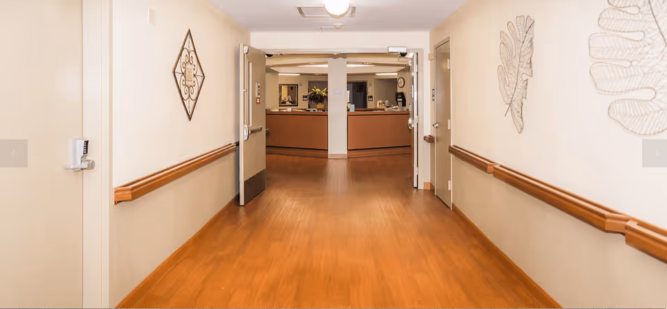 Interior hallway with wood flooring, wall handrails and open double doors leading to a reception desk.