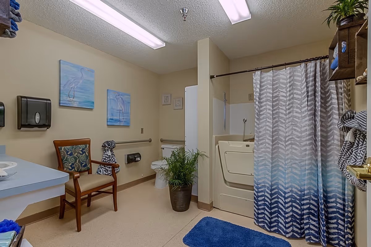 Accessible bathroom with a walk-in tub and shower curtain, toilet, sink, chair, and wall art.