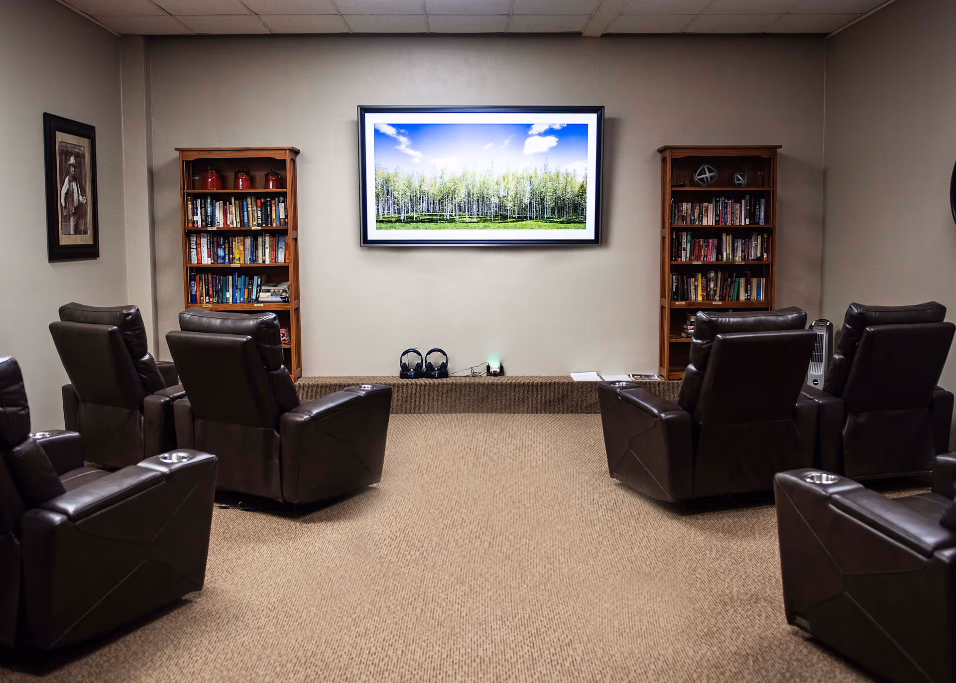 A media lounge with leather recliners arranged facing a wall-mounted TV flanked by bookshelves.