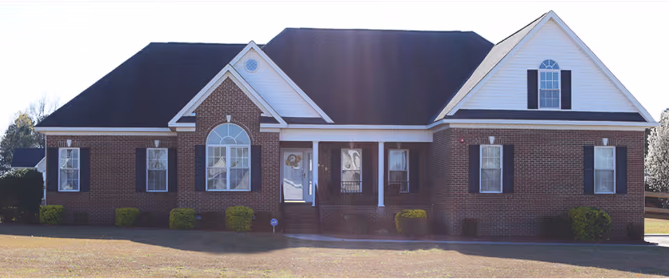 Front exterior of a one-story brick house with a gabled roof, arched central window and small covered porch on a lawn.