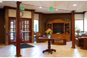 Bright lobby-style common area with wooden columns, leather seating, a TV cabinet, and double glass entry doors.