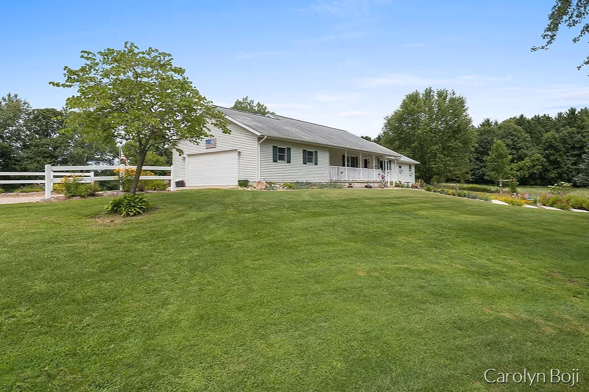 Single-story white house with an attached garage and front porch set on a large green lawn with trees.