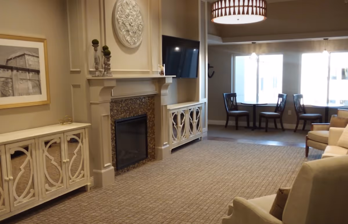 Common area with a fireplace and mounted TV, decorative cabinets, seating and a small table by windows.