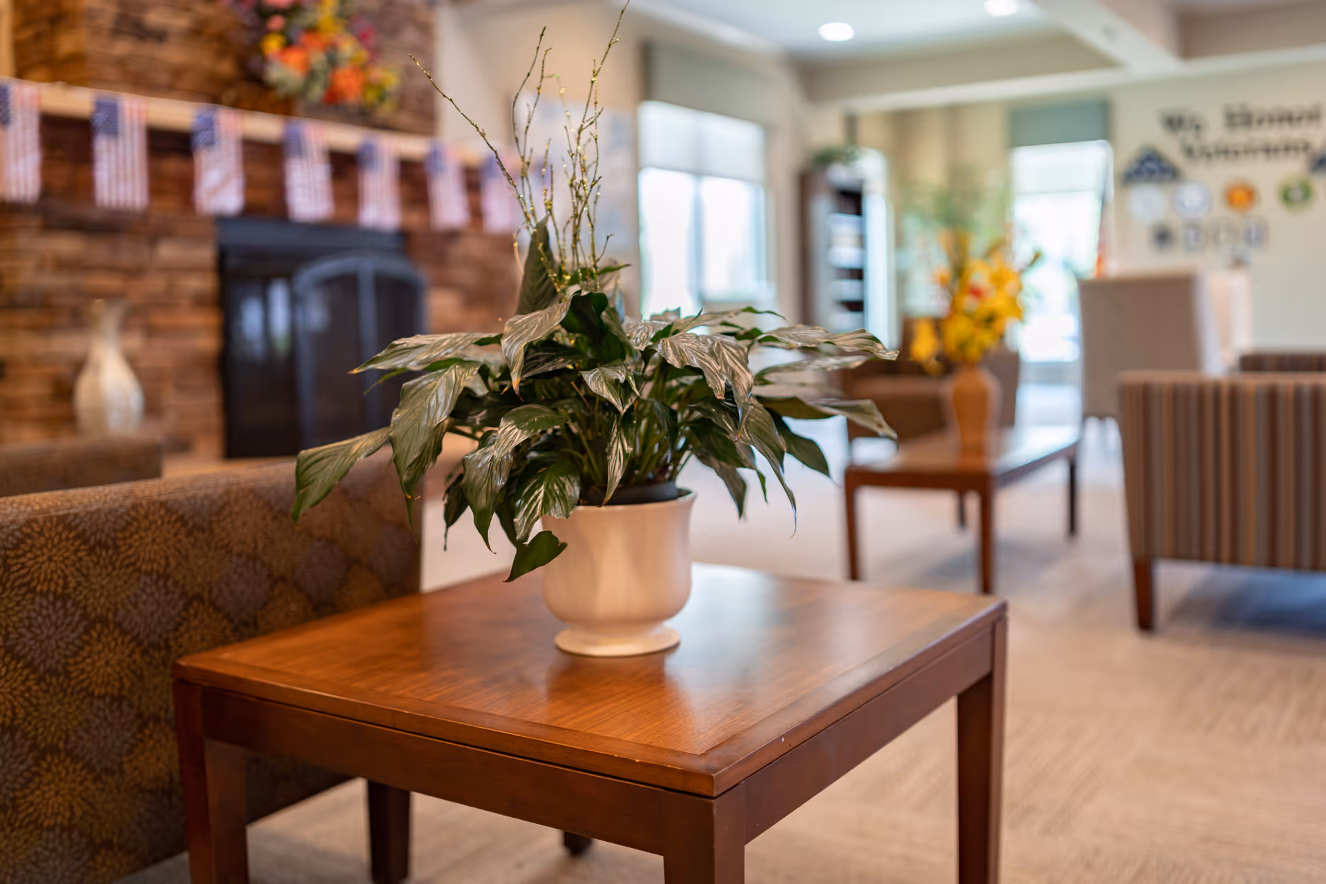 A cozy communal lounge with a potted plant on a wooden side table, seating, and a stone fireplace in the background.