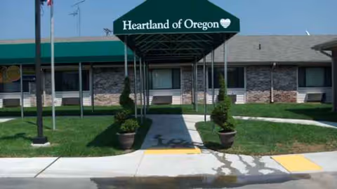 Entrance to a senior living facility with green canopy and potted plants.