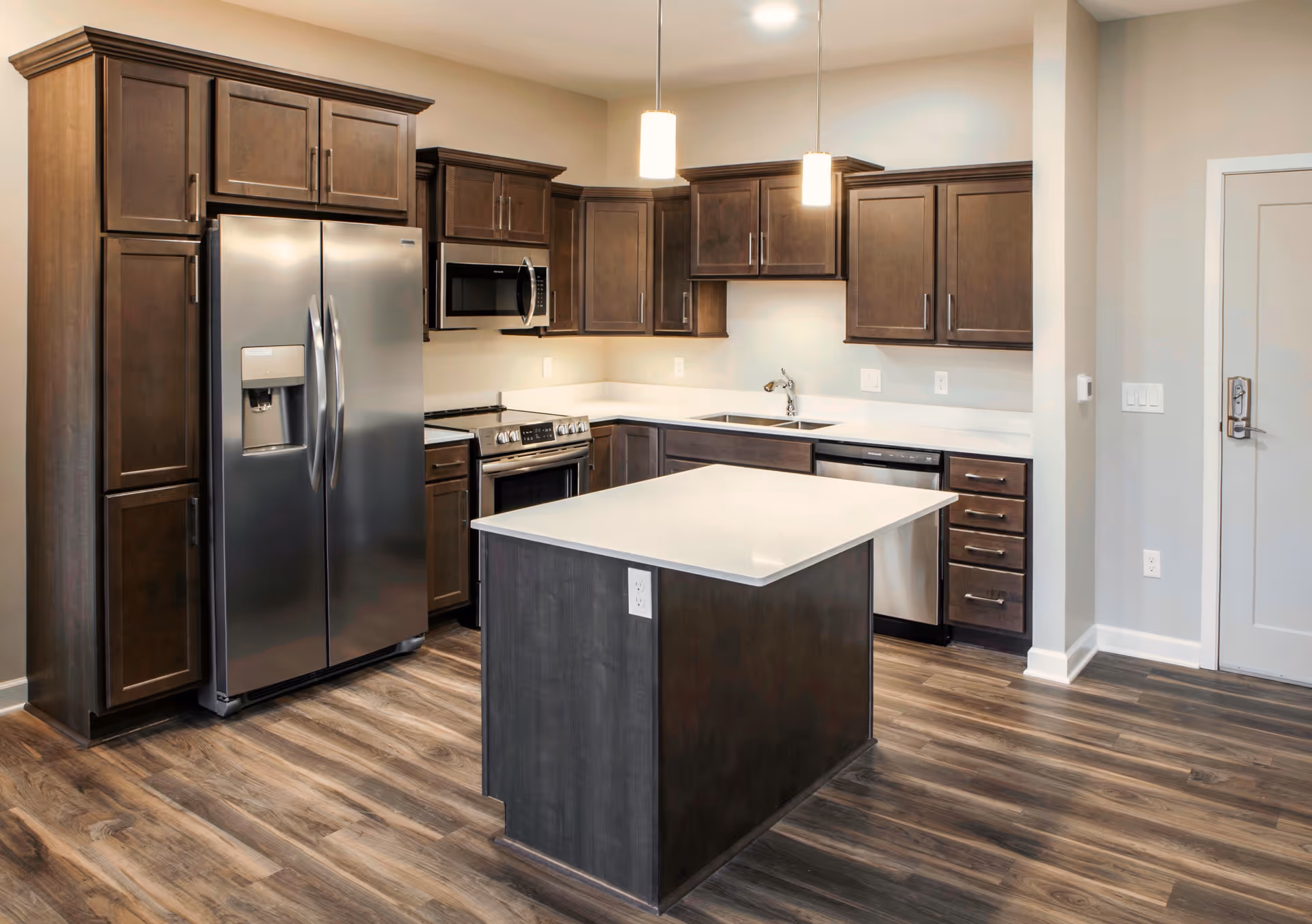 Modern kitchen with dark wood cabinets, stainless steel appliances, a central island, and wood-look flooring.