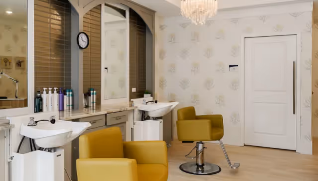 A bright salon interior with yellow styling chairs, two shampoo sinks, mirrors, and a countertop with hair products.