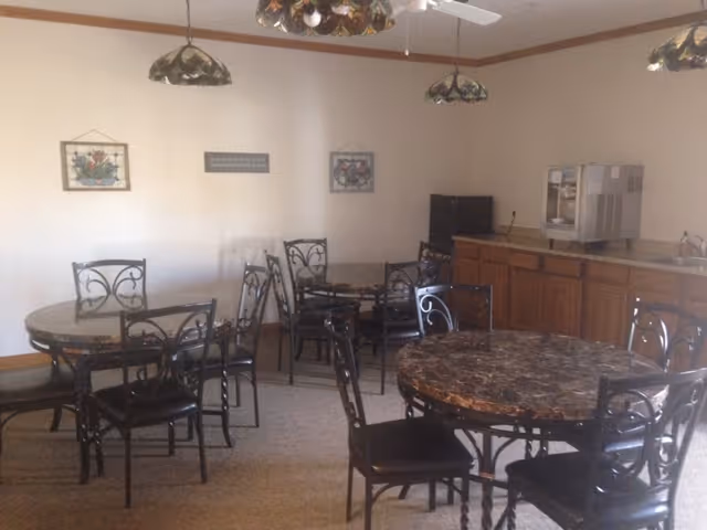 Small dining room with several round marble-top tables, metal chairs, pendant lights, and a service counter with cabinets.