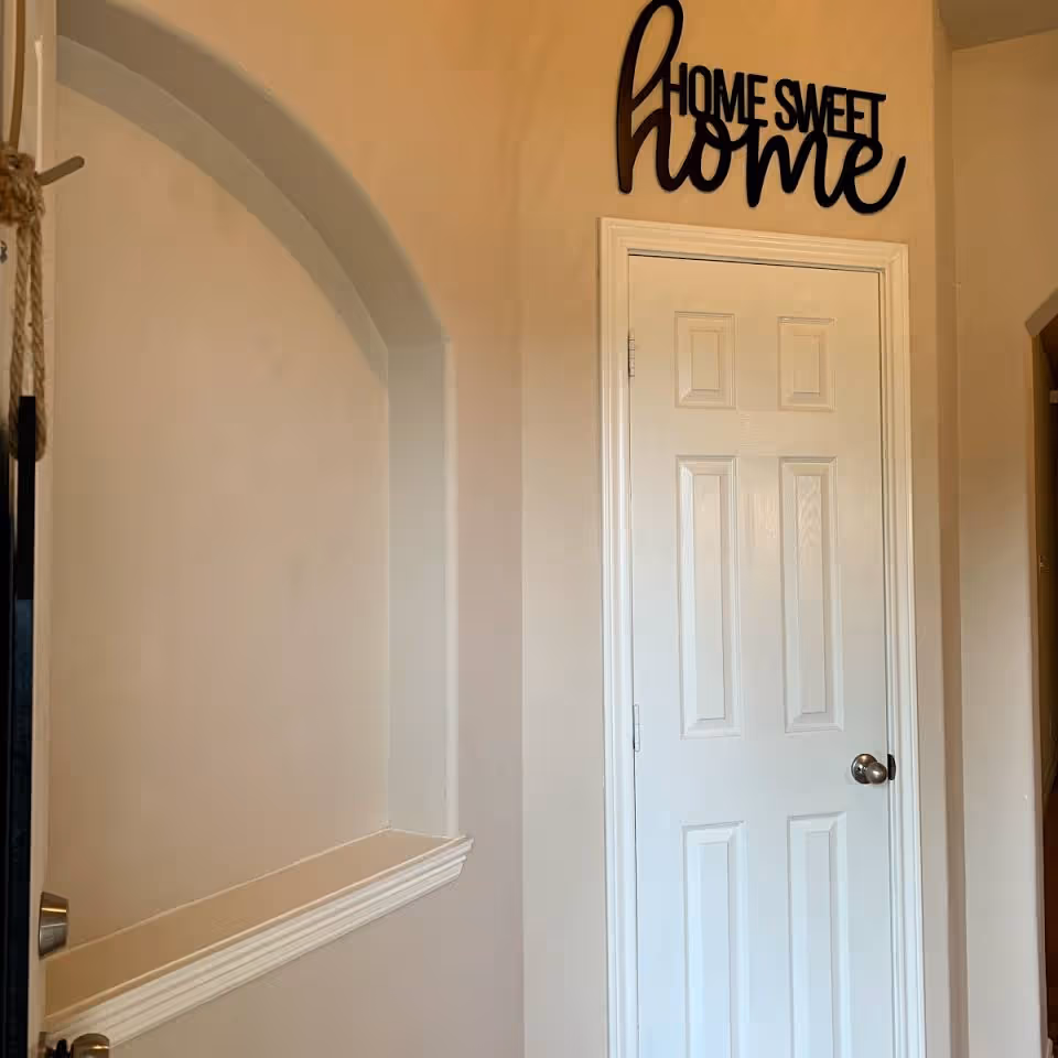 Interior hallway with a closed white paneled door, an arched wall niche, and a "Home Sweet Home" sign above the door.