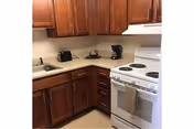 Compact kitchen with wooden cabinets, a white electric stove, sink, and countertop appliances (toaster and coffee maker).