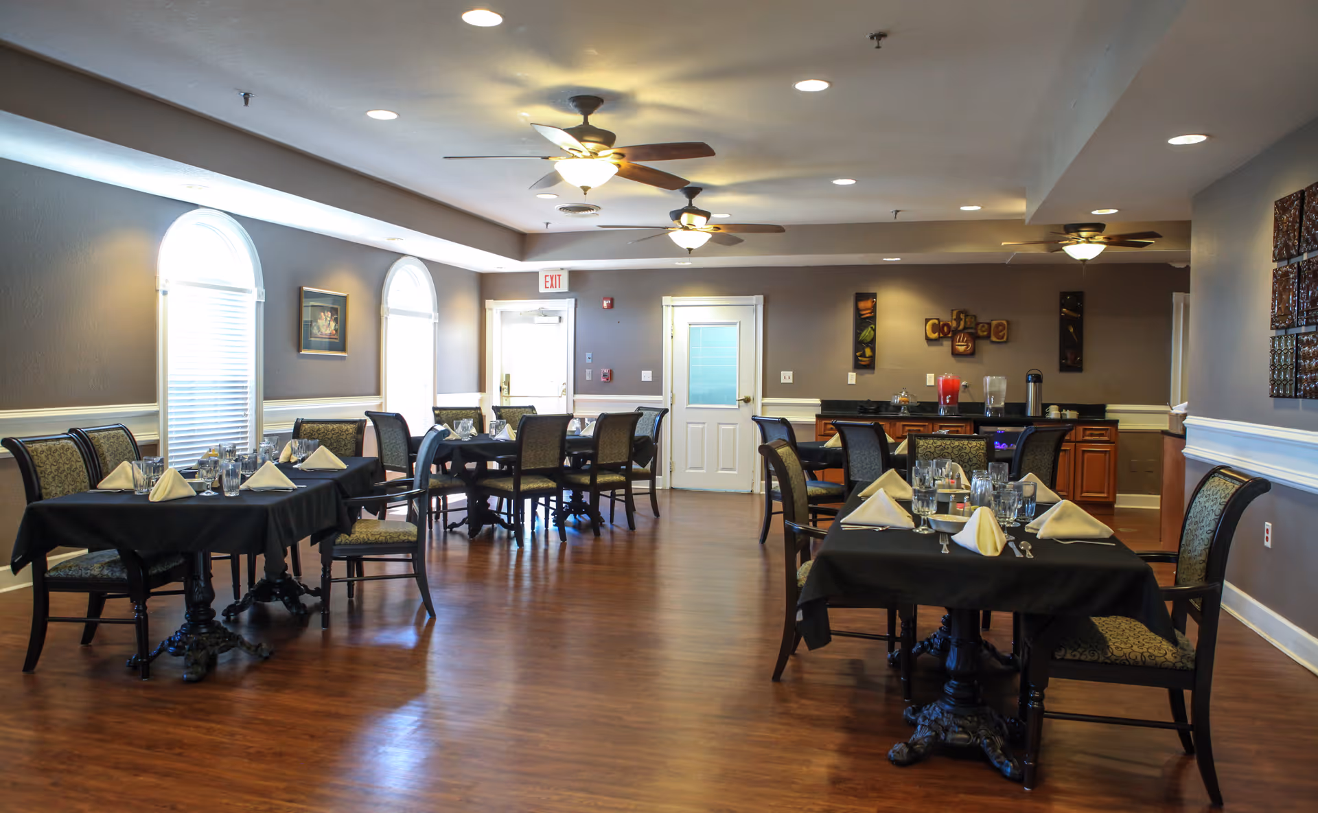 Spacious communal dining room with multiple set tables and chairs, ceiling fans, and a service counter.