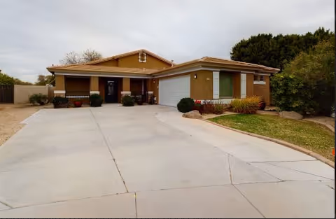 Single-story assisted living facility with driveway, shrubs, and a two-car garage.